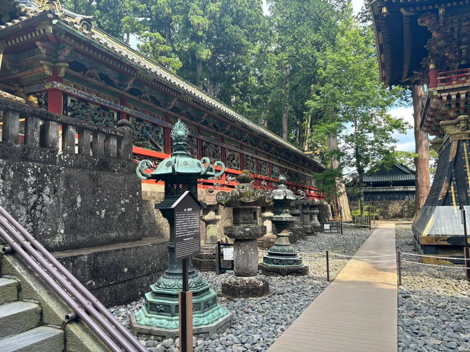Camino de piedra en Nikkō con linternas de bronce, rodeado de templos tradicionales y naturaleza.