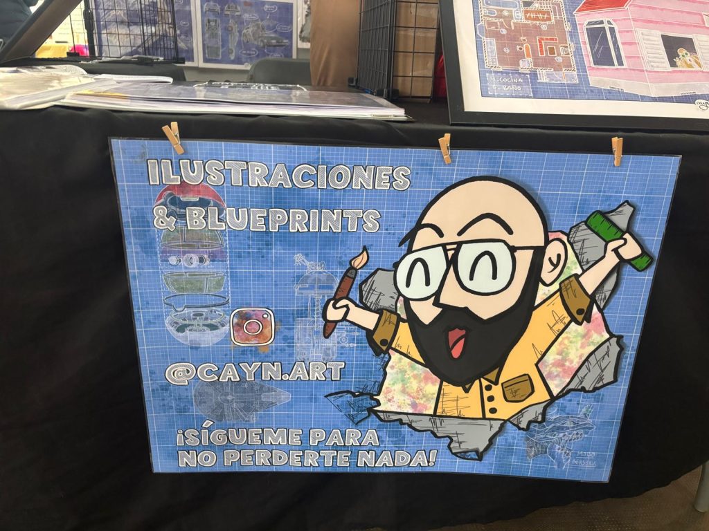 Cartel promocional del artista Cayn.Art en su stand del Salón del Manga de Calella, con su logotipo y redes sociales